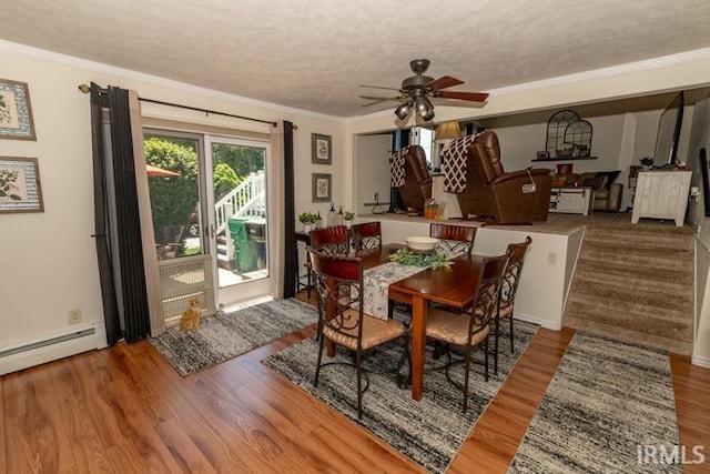 dining space with ceiling fan, baseboard heating, hardwood / wood-style floors, a textured ceiling, and ornamental molding