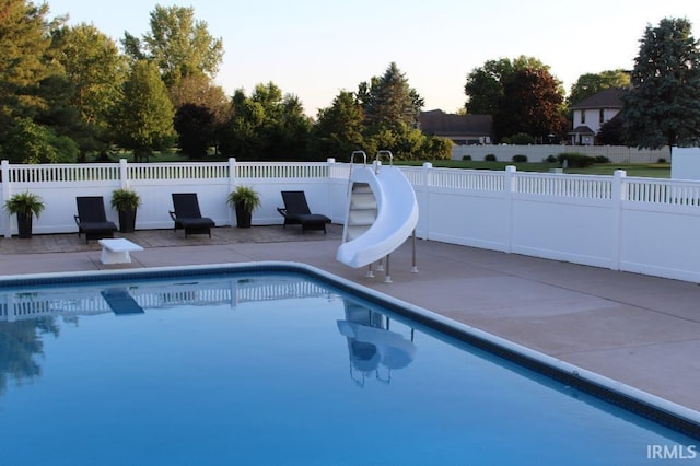 pool at dusk with a patio area and a water slide