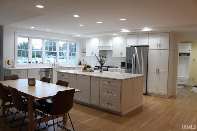 kitchen with a center island, premium range hood, white cabinets, light wood-type flooring, and stainless steel appliances