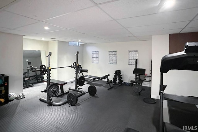 exercise room featuring a paneled ceiling and baseboards