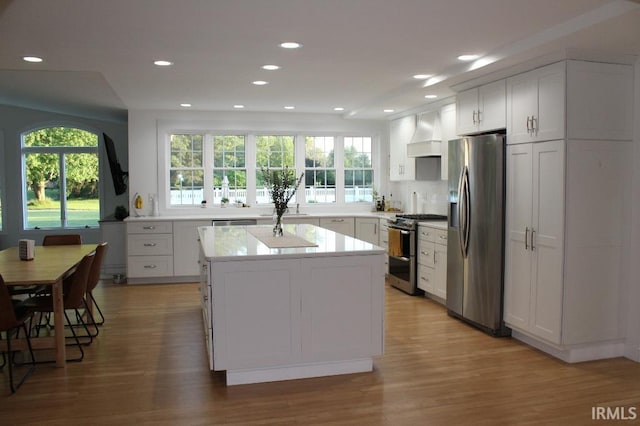 kitchen with a wealth of natural light, appliances with stainless steel finishes, white cabinetry, and custom range hood