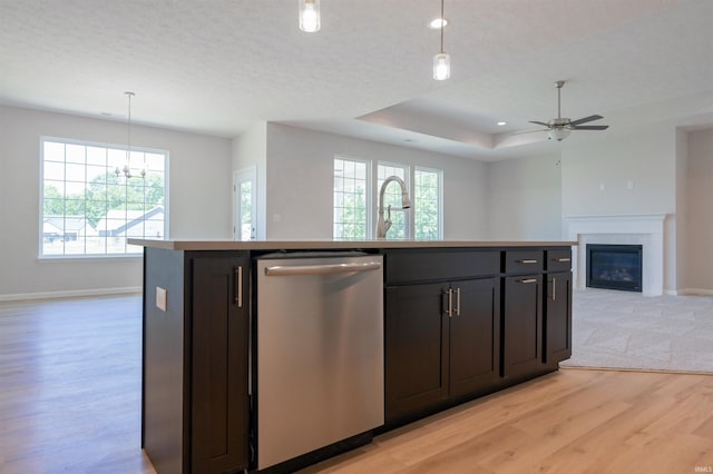 kitchen with a center island with sink, hanging light fixtures, stainless steel dishwasher, a tray ceiling, and light hardwood / wood-style floors