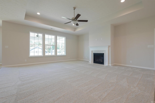 unfurnished living room with ceiling fan, a raised ceiling, and light colored carpet