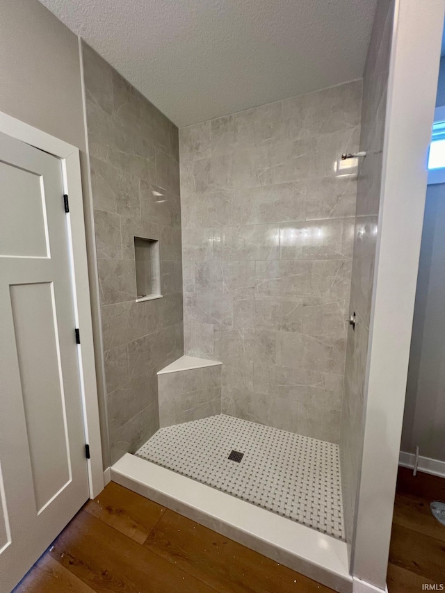 bathroom with tiled shower and wood-type flooring