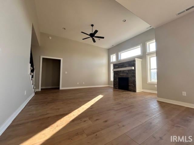 unfurnished living room with a towering ceiling, hardwood / wood-style flooring, a stone fireplace, and ceiling fan