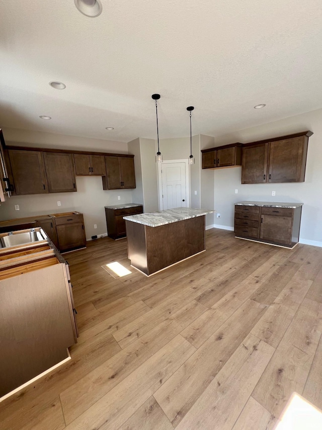 kitchen featuring pendant lighting, light hardwood / wood-style flooring, a kitchen island, and dark brown cabinets