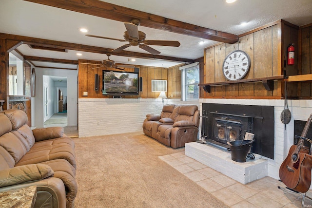 carpeted living room with beam ceiling, ceiling fan, and wood walls