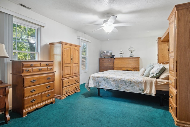 bedroom with ceiling fan, dark carpet, multiple windows, and a textured ceiling