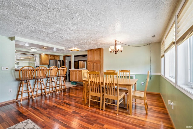 dining room with a textured ceiling, dark wood-type flooring, and a notable chandelier