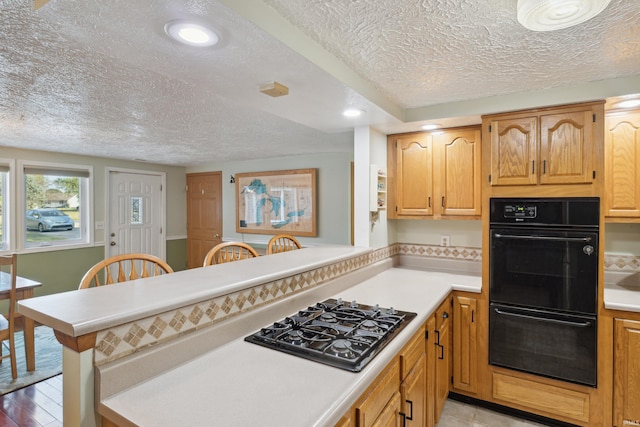 kitchen with a textured ceiling, black double oven, stainless steel gas cooktop, and kitchen peninsula