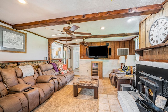 living room featuring beamed ceiling, a wood stove, a textured ceiling, ceiling fan, and light carpet