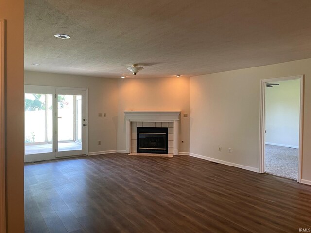 unfurnished living room featuring a tile fireplace, a textured ceiling, and dark wood-type flooring