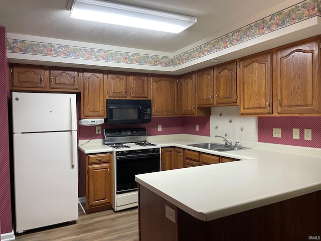 kitchen featuring light hardwood / wood-style flooring, white appliances, kitchen peninsula, sink, and tasteful backsplash