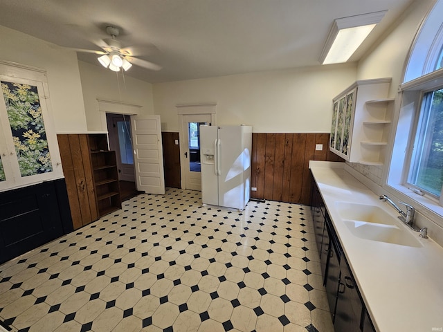 kitchen with ceiling fan, white fridge with ice dispenser, sink, and wooden walls