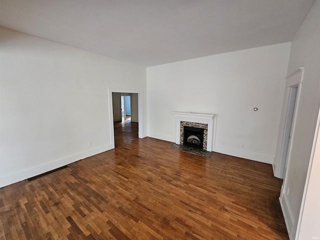 unfurnished living room featuring a stone fireplace and dark hardwood / wood-style floors