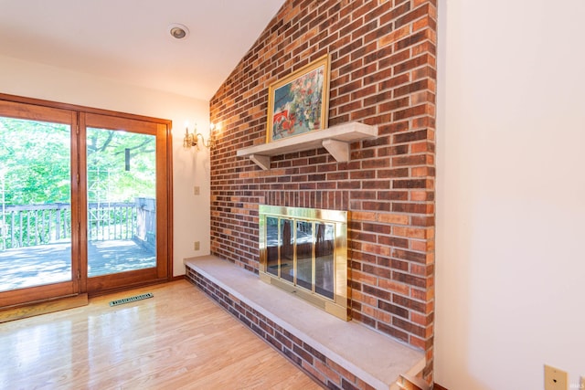 unfurnished living room with brick wall, a fireplace, lofted ceiling, and light wood-type flooring