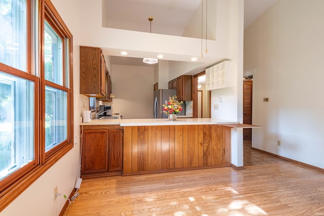 kitchen featuring kitchen peninsula, light wood-type flooring, a towering ceiling, a wealth of natural light, and stainless steel refrigerator