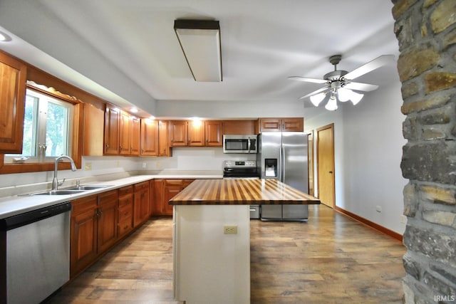 kitchen with appliances with stainless steel finishes, sink, light hardwood / wood-style flooring, a center island, and butcher block countertops