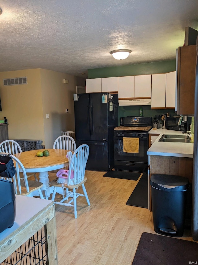 kitchen with a textured ceiling, black appliances, light hardwood / wood-style floors, sink, and white cabinetry