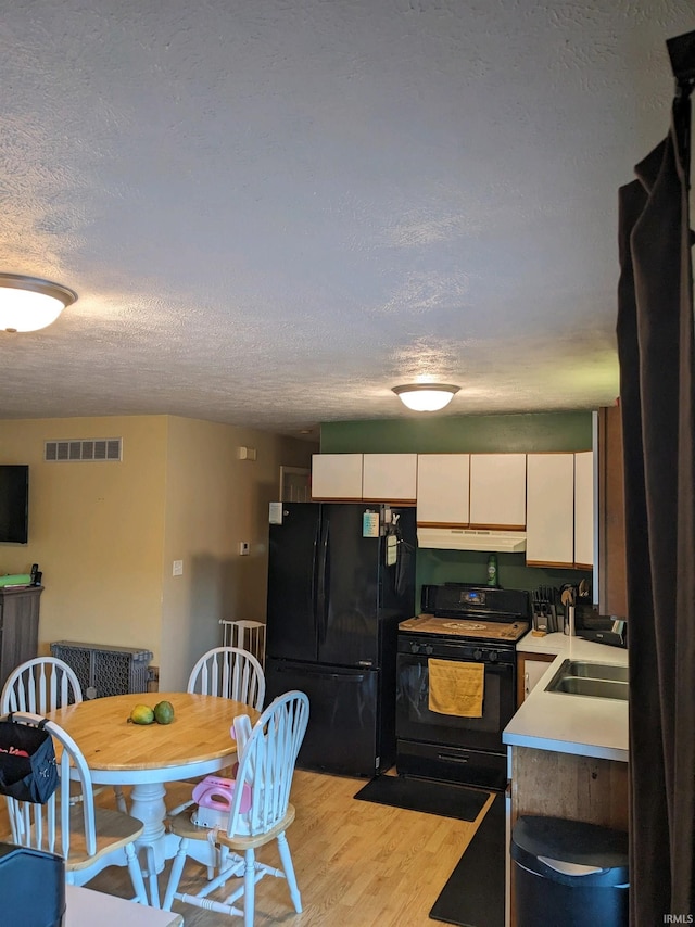 kitchen with white cabinets, light wood-type flooring, sink, black appliances, and a textured ceiling