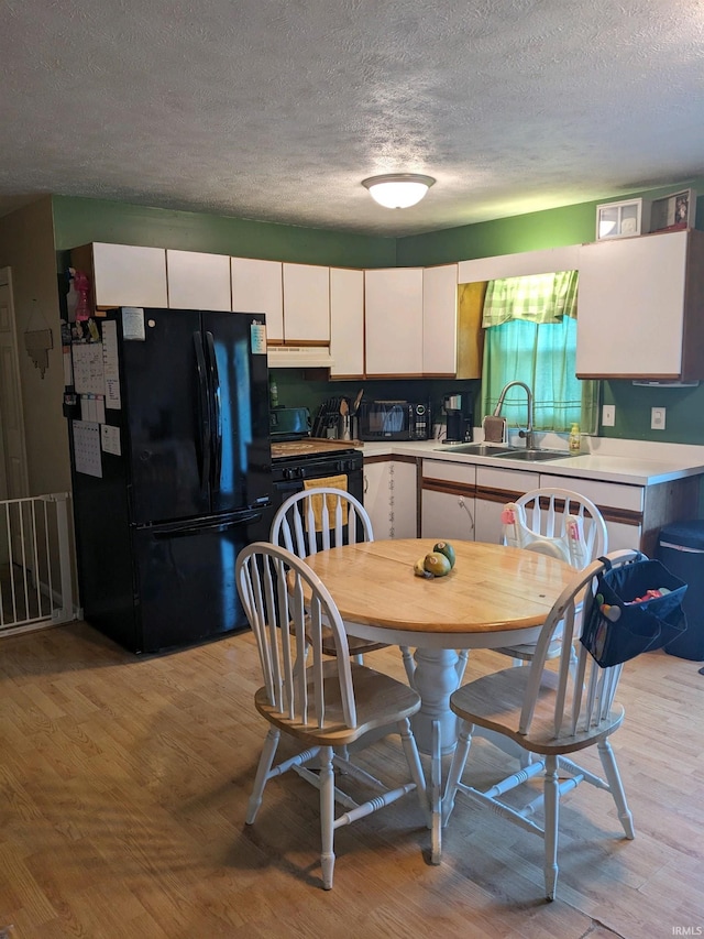 kitchen featuring a textured ceiling, black refrigerator, sink, white cabinets, and light hardwood / wood-style floors