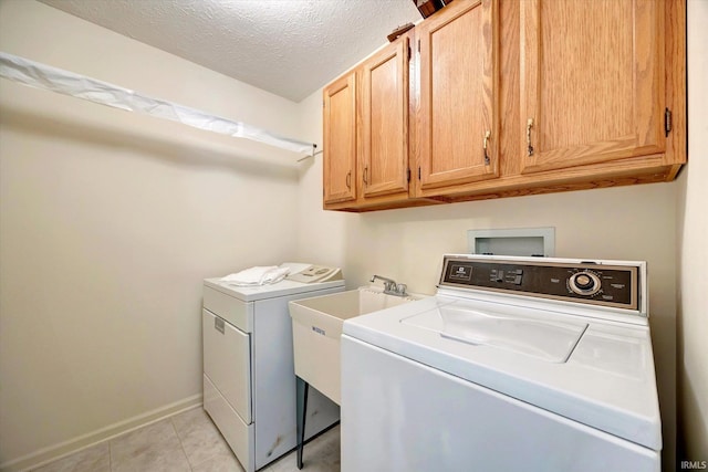 laundry area featuring washing machine and clothes dryer, cabinet space, light tile patterned flooring, a textured ceiling, and baseboards