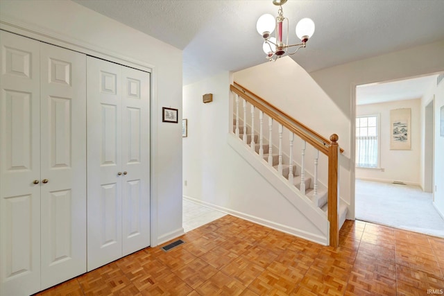 stairway featuring a textured ceiling, baseboards, visible vents, and an inviting chandelier