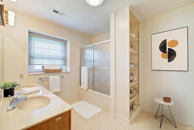 bathroom with shower / bath combination with glass door, a sink, visible vents, tile patterned floors, and double vanity