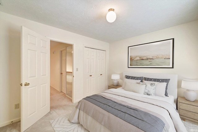 bedroom with light carpet, a closet, a textured ceiling, and baseboards