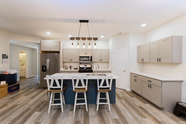 kitchen with sink, hanging light fixtures, an island with sink, appliances with stainless steel finishes, and light wood-type flooring