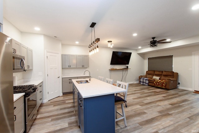 kitchen with ceiling fan, hanging light fixtures, stainless steel appliances, a kitchen breakfast bar, and a center island with sink