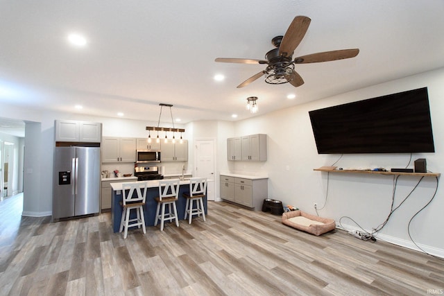 kitchen featuring appliances with stainless steel finishes, a kitchen breakfast bar, gray cabinetry, ceiling fan, and hanging light fixtures