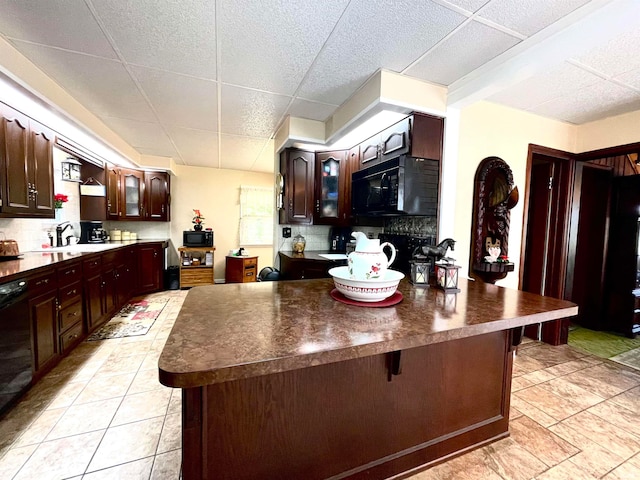 kitchen featuring a breakfast bar, light tile flooring, a paneled ceiling, and black appliances