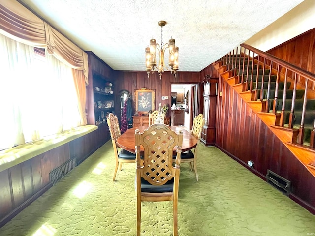 dining area featuring an inviting chandelier, carpet, a textured ceiling, and wood walls