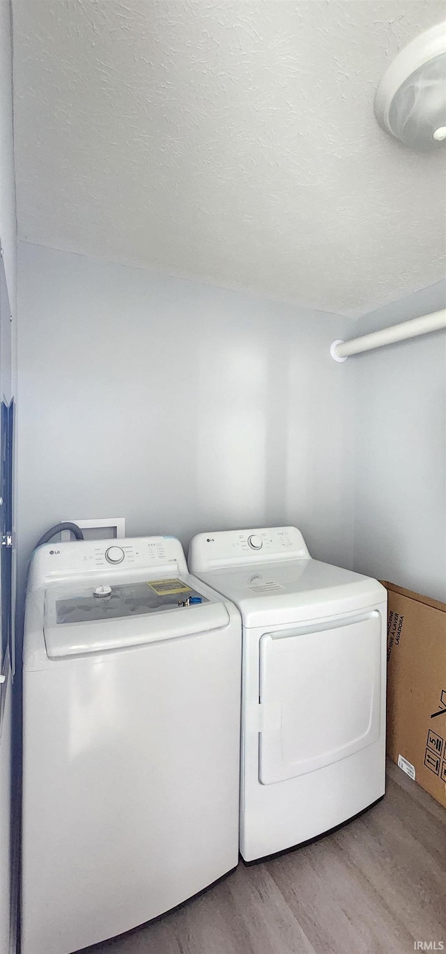 clothes washing area with a textured ceiling, washer and dryer, and light hardwood / wood-style flooring