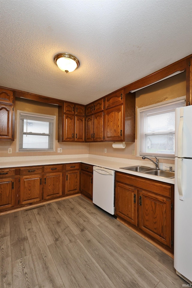 kitchen featuring a textured ceiling, light hardwood / wood-style flooring, white appliances, and sink