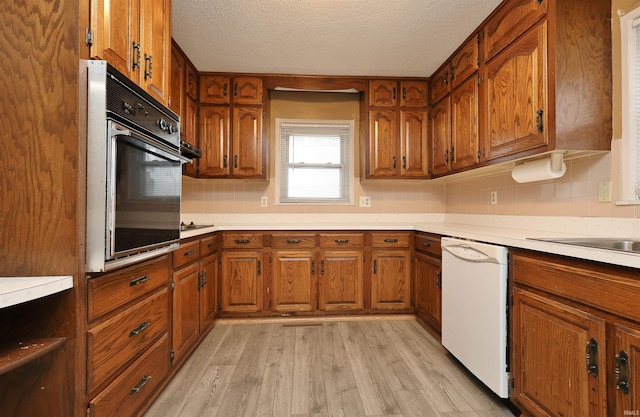 kitchen with white dishwasher, oven, light wood-type flooring, and a textured ceiling