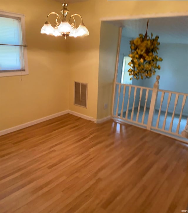 empty room featuring a notable chandelier and wood-type flooring