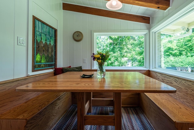 dining space with breakfast area, lofted ceiling with beams, plenty of natural light, and wooden walls