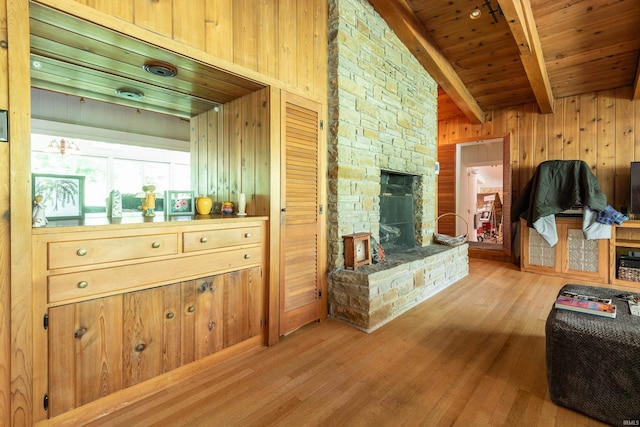 living room featuring wooden ceiling, a stone fireplace, wooden walls, and light hardwood / wood-style floors