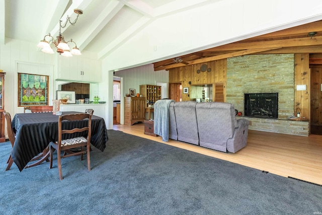 living room with a stone fireplace, beamed ceiling, wood-type flooring, wooden walls, and ceiling fan with notable chandelier