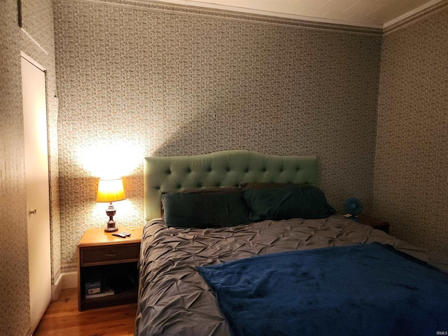 bedroom featuring wood finished floors, crown molding, and wallpapered walls