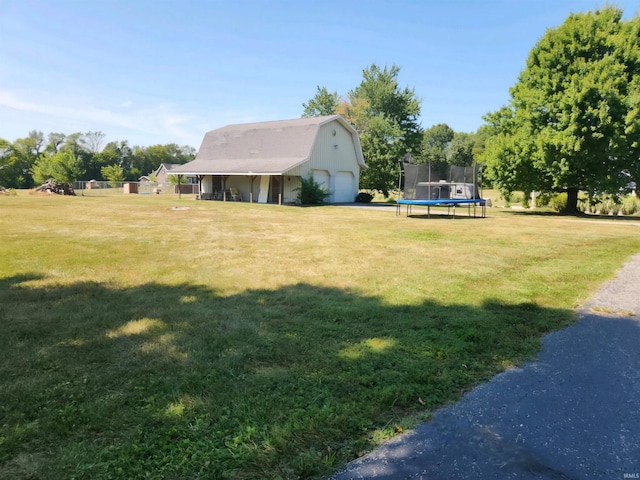 view of yard featuring a garage, a trampoline, and an outbuilding