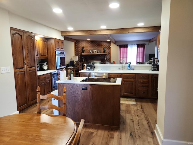 kitchen with black electric stovetop, light wood finished floors, light countertops, a sink, and beamed ceiling