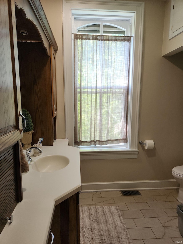 half bath featuring toilet, visible vents, vanity, baseboards, and tile patterned floors