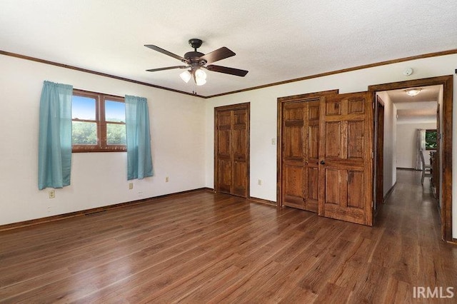 unfurnished bedroom featuring a textured ceiling, dark hardwood / wood-style flooring, two closets, and ceiling fan