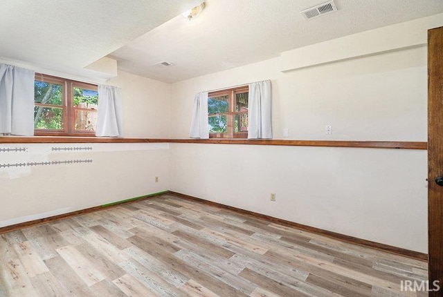 unfurnished room featuring a healthy amount of sunlight, a textured ceiling, and light hardwood / wood-style floors