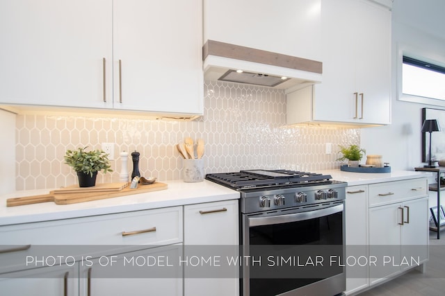 kitchen with decorative backsplash, stainless steel range with gas cooktop, white cabinets, and custom exhaust hood