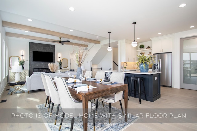 dining room featuring beam ceiling, ceiling fan, a large fireplace, and sink