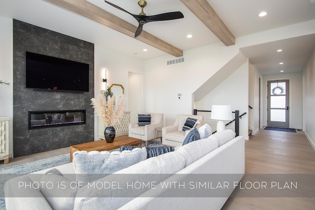 living room featuring beamed ceiling, light hardwood / wood-style floors, ceiling fan, and a premium fireplace